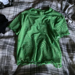 Grön mönstrad mesh topp NLY Trend - Säljer en grön mesh topp från NLY Trend i storlek M. Toppen har ett coolt psykedeliskt mönster i olika gröna nyanser och vågiga kanter vid ärmar och nederkant. Materialet är tunn och stretchig polyester, perfekt för att sticka ut i mängden.
