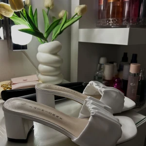 Vita sandaler med klack och rynkad rem - Snygga vita sandaler med fyrkantig tå och låg blockklack. Skorna har en bred, rynkad rem över foten i mjukt syntetmaterial. Perfekta för dig som vill ha en stilren men trendig look med en twist.