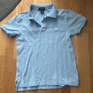 Ljusblå Polo Ralph Lauren t-shirt - Snygg ljusblå t-shirt från Polo Ralph Lauren med klassisk pikékrage och korta ärmar. Broderad vit logga på bröstet och custom fit-passform. Perfekt för dig som gillar stilrena och tidlösa plagg. Materialet är mjuk bomull som andas.