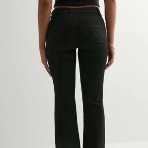 Svarta bootcut jeans med låg midja - Säljer ett par svarta jeans med bootcut-modell och låg midja. Jeansen har klassiska fem fickor, bälteshällor och snygga sömdetaljer på bakfickorna. Perfekta för dig som gillar en tidlös och clean look.