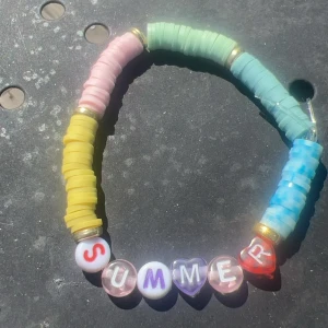 Färgglatt handgjort armband med SUMMER-pärlor - Armband med pastellfärgade platta pärlor i blått, grönt, gult och rosa samt bokstavspärlor som stavar SUMMER. Några pärlor är hjärtformade och transparenta. Perfekt accessoar för dig som älskar färg och sommarkänsla.