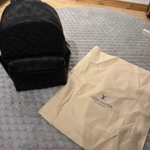 Svart Louis Vuitton ryggsäck i skinn - Säljer en svart ryggsäck från Louis Vuitton med klassiskt monogrammönster. Väskan är tillverkad i skinn och har en rundad form med en stor ytterficka med dragkedja. Justerbara axelremmar och handtag upptill. Perfekt för dig som gillar lyxiga detaljer.