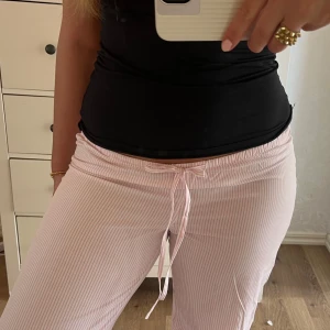 Rosa randiga mjukisbyxor med snörning - Säljer ett par ljusrosa mjukisbyxor med vita ränder och snörning i midjan. Byxorna har låg midja och raka ben, perfekta för hösten. Pyjamasbyxorna är helt nya med prislappen kvar💌så så fina. Säljer för att de är lite små på mig 🥲