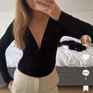 Svart omlott body med v-ringning - Svart långärmad omlott body med djup v-ringning. Sitter tight och har en stilren, minimalistisk look som passar perfekt till både jeans och kostymbyxor. Tunn och stretchig, vilket gör den superbekväm och enkel att styla.