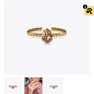Caroline svedbom Vintage rose ring - Snygg guldfärgad ring med twistad band och en droppformad rosa sten i mitten. Ringen har en elegant och modern look som sticker ut på handen. Perfekt för dig som gillar unika detaljer och vill ha något som syns.