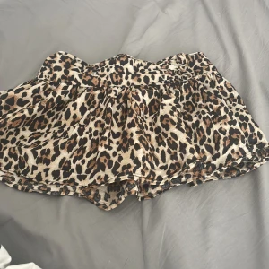 Leopardmönstrad kortkjol med volang - Säljer en superfin kortkjol med leopardmönster i beige, brunt och svart. Kjolen har en volangig och luftig form med resår i halva midjan för extra komfort. Perfekt för dig som vill sticka ut med en trendig look.