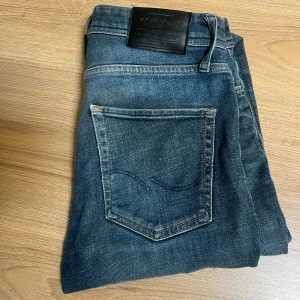 Blå jeans från Jack & Jones Regular Clark - Snygga blå jeans från Jack & Jones, modellen Regular Clark (sitter lite som replay anbass fast lite mer avslappnat). Klassisk femficksdesign med raka ben och normal passform. Jeansen har en mörk tvätt med subtila slitningar och detaljerade sömmar på bakfickorna. Perfekta för en chill och stilren look. Passar perfekt på mig och jag är 180cm och stax under 60kg. De ba att höra av sig vid minsta lilla fundering👑