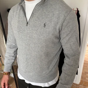 Grå half zip tröja från Polo Ralph Lauren - Snygg grå långärmad tröja från Polo Ralph Lauren med half zip och klassisk logga broderad på bröstet. Använd ett fåtal gånger, kommer i mycket bra skick. 