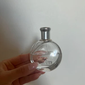 Hollister parfym rund flaska - Fräsch parfym från Hollister i en rund, genomskinlig glasflaska med silverfärgad kork. Flaskan har en stilren design med Hollister-loggan tryckt på framsidan. Perfekt för dig som gillar en enkel och snygg look på parfymhyllan.