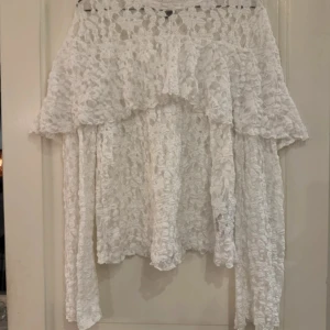 Vit spetsblus med volang från Gina Tricot  - Superfin vit blus i spets med lång ärm och bred volang över axlarna. Blusen är ganska genomskinlig och har en romantisk känsla med sitt blommiga spetsmönster. 🥰