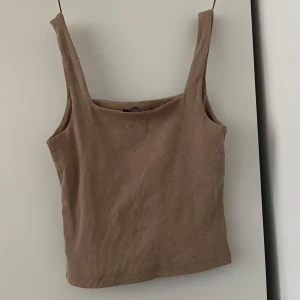 Beige ribbad linnetopp - Säljer en beige ribbad linnetopp med breda axelband och fyrkantig ringning. Toppen är croppad och har en enkel, stilren look som passar perfekt till jeans eller kjol. Materialet är mjukt och stretchigt för en bekväm passform.