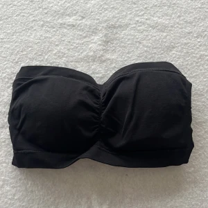 Svart bandeau topp från Magic Bodyfashion - Svart bandeau topp från Magic Bodyfashion, perfekt för dig som vill ha en enkel och stilren tubtopp. Modellen är axelbandslös och har lätt rynkning framtill för snygg passform. Tillverkad i mjukt och stretchigt syntetmaterial för maximal komfort.