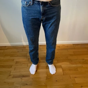 Blå relaxed jeans från & Denim - Säljer ett par blå jeans från & Denim i relaxed fit. Modellen har klassisk femficksdesign, rak passform och normal midja. Jeansen är tillverkade i slitstark denim och har en enkel, tidlös look som funkar till många stilar. Jag är 191cm