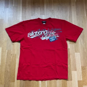 Vintage Billabong Röd T-Shirt - Vintage Billabong T-Shirt med tryck i färgen röd. Storlek: XL, Armhåla till Armhåla: 57 cm, Längd: 71 cm, Axel till Armöppning: 26 cm.  Material: 100% Cotton.