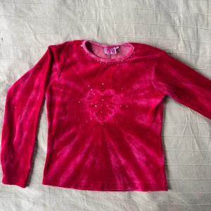 Röd långärmad tröja med hjärtmönster - Cool röd långärmad tröja med tie-dye och hjärtmönster i mitten. Framsidan har små paljetter runt halsen och på hjärtat. Från Indiska och är i barnstorlek 146/152 men passar om en XS. 