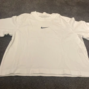 Vit loose fit t-shirt från Nike - Säljer en vit t-shirt från Nike med klassisk svart swoosh-logga på bröstet. Modellen är loose fit och har korta ärmar. Tillverkad i mjuk bomull som känns skön mot huden. Perfekt för en avslappnad och sportig stil.