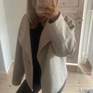 Beige kappa från 157, st. XS - Snygg beige kappa från 157 i storlek XS. Jackan har en oversized krage, dubbelknäppning framtill och raka fickor. Tillverkad i ullblandning med slät insida. Säljer pga har för många jackor!