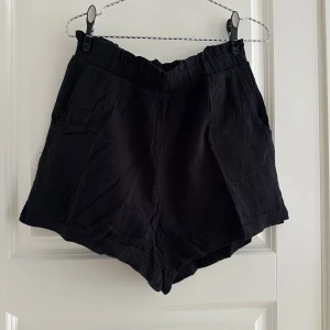 Svarta bomullsshorts från Vero Moda - Svarta shorts från Vero Moda i mjuk, lätt och luftig bomull. De har elastisk midja och två sidofickor, perfekt för chill dagar. Modellen är loose fit och materialet har en lätt skrynklig struktur som ger en avslappnad vibe.