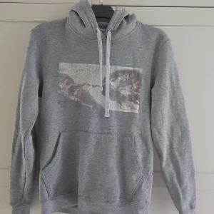 Grå hoodie The Cool Elephant konsttryck - Grå hoodie från The Cool Elephant med konstinspirerat tryck framtill. Tröjan har huva med snörning, känguruficka och långa ärmar. Mjuk insida och klassisk passform, perfekt för chill dagar. Materialet är troligtvis bomullsmix.