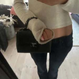 Mörkgrå handväska med nitar och struktur - Snygg mörkgrå handväska med reptilstruktur och coola nitar på handtaget. Väskan har ett metallspänne framtill och en kompakt, boxig form som ger en edgy vibe. Perfekt storlek för det viktigaste och passar till många olika stilar.