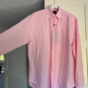 Ljusrosa linneskjorta Oscar Jacobson - Fräsch ljusrosa skjorta från Oscar Jacobson i linne, regular fit med klassisk krage och snygga knappar. Perfekt för dig som vill ha en chill och stilren look. Långärmad och riktigt skön på sommaren. Oanvänd med orginalförpackning samt lappar kvar. 