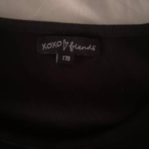 Svart kortärmad klänning XOXO Friends - En svart, enkel och tight kortklänning från XOXO Friends. Klänningen har korta ärmar och en lätt rynkad detalj på ena sidan. Perfekt för dig som gillar en stilren look med en liten twist.