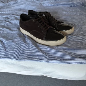 Lanvin - Snygga bruna sneakers från Lanvin med coola svarta lackade tår och vita sulor. Skorna har snörning och en klassisk rund tå. Perfekta för dig som gillar en stilren men ändå unik look.