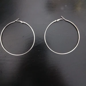 Stora silverfärgade hoops örhängen - Säljer ett par stora, klassiska hoops i silverfärg. De är tunna och runda med smidig låsmekanism, perfekta för att ge en clean och stilren vibe till din look. Passar dig som gillar minimalistiska smycken med lite edge. Har aldrig använts men har tyvärr inte kvittot:)