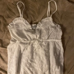 Vit topp med broderade detaljer - Supersöt vit topp med smala axelband, volangkant upptill och knyt. Jätte fin topp som tyvärr inte passar mig 