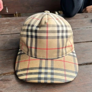 Burberry keps  - Använd runt 6 månader, allt ser bra ut på den bara knapparna där bak har gått sönder men 2 knappar gå o stänga. Kepsen går utan box o kvitto