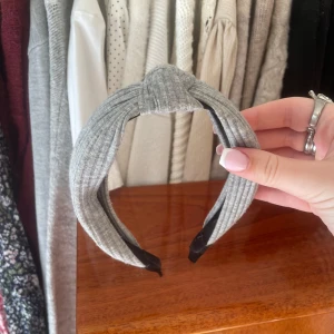 Grått ribbat diadem - Säljer ett snyggt grått diadem med ribbad struktur och twistad knut framtill. Perfekt accessoar för att lyfta din outfit. Bekväm passform och stilren design.