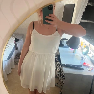 Vit kortklänning från BikBok - Säljer en söt vit kortklänning från BikBok med smala axelband och lätt, flowigt tyg. Perfekt för varma dagar och enkel att styla med accessoarer. Klänningen har en avslappnad passform och är superbekväm.