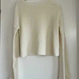 Vit stickad croppad tröja från NA-KD - Säljer en vit stickad tröja från NA-KD. Tröjan har lång ärm och en enkel, klassisk design med rund halsringning. Perfekt till sommarens kvällar.