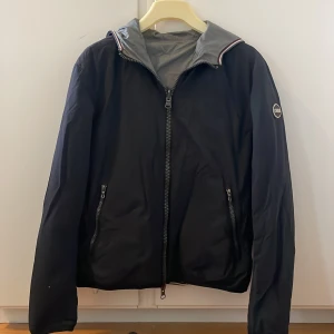 Svart/grå vindjacka från Colmar - Snygg svart vindjacka som även är ut och invändbar för att ändra färgen till en grå jacka. Jackan är ifrån märket Colmar med huva och dragkedja framtill. Jackan har två fickor med dragkedja och Colmar-logga på ärmen. Perfekt för blåsiga dagar och enkel att matcha med olika outfits. Den är bra skick men dragkedjan är lite krånglig! Kom privat vid fler frågor!