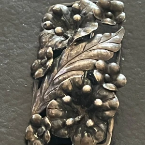 Vintage brosch i silver med blommotiv1930s - Unik rektangulär brosch i silver med detaljerat blommotiv och blad. Vackert handarbetad med tredimensionella blommor och bär, perfekt som accessoar för att lyfta din outfit.