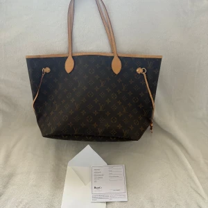 Louis Vuitton Monogram Neverfull handväska - Säljer en klassisk Louis Vuitton Neverfull handväska i brunt monogrammönster med ljusbruna läderhandtag. Väskan har rymligt innandöme med innerficka och dragkedja. Perfekt för dig som vill ha en ikonisk accessoar med lyxig känsla.