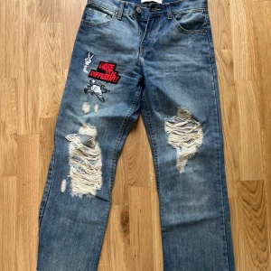 Blå jeans med tryck och slitningar - Boyfriend jeans stolen 34 från pink women. Säljer ett par blå jeans med stora slitningar på båda benen och tryck på vänster lår där det står 'Dare 2B Different' samt en tecknad figur. På baksidan finns ett litet tryck vid ena bakfickan. Jeansen har klassisk femficksdesign och rak passform. Lite Cropped i designen nedtill 