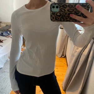 Vit långärmad topp - Säljer en enkel och stilren vit långärmad topp med rund halsringning. Modellen är tight och passar perfekt till både jeans och kjol. Materialet känns mjukt och stretchigt, vilket gör den bekväm att bära hela dagen.