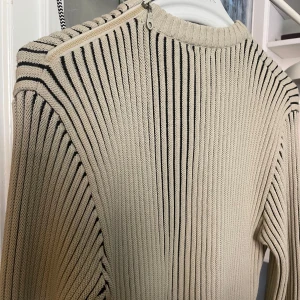 “Dolce Gabbana” ribbad tröja - Supersnygg Dolce Gabbana tjocktröja. Ribbad med skiftningar mellan svart och ljusbeige/grå. Liten dragkedja vid axeln, logo på armen och silvrig & märke på sidan. Köpte second hand, vet ej om äkta.