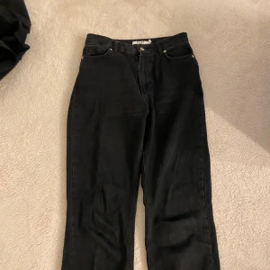 Svarta jeansbyxor från NA-KD - Säljer ett par svarta jeansbyxor från NA-KD i klassisk femficksmodell. Byxorna har raka ben och normal passform, perfekta till många olika outfits. Stängs med dragkedja och knapp i midjan.