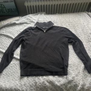 Svart stickad tröja med halv dragkedja från 157 - Säljer en svart stickad tröja från 157 med halv dragkedja i halsen. Tröjan har lång ärm och ribbade muddar vid ärmslut och nederkant. Perfekt för kyligare dagar och enkel att matcha med olika outfits.
