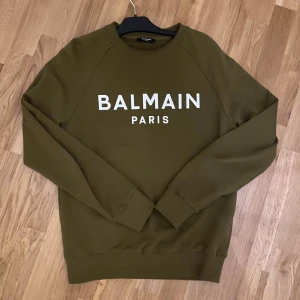 Olivgrön sweatshirt från Balmain Paris - Säljer en tröja från Balmain Paris. Spontan köp på NK, har haft på mig den 3 gånger. Nytt pris ligger ute för 6000kr men vill ba få bort den från garderoben då jag inte använder den. Den är storlek S och är perfekt för en stilren och avslappnad look.