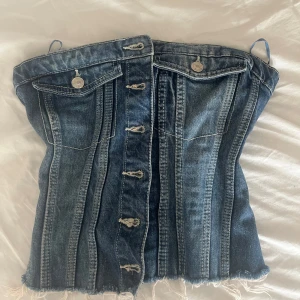 Jeans korsett-topp från zara - Säljer en snygg korsett-topp i jeans med knappar framtill och dekorativa sömmar. Toppen har två fickor med lock och silverfärgade knappar. Perfekt för att skapa en cool och trendig look. Sitter som S