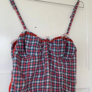 Rutig linnetopp med knytband - Säljer en rutig linnetopp i blått, rött och vitt med smala axelband och knytband i sidan. Toppen har en söt volangkant upptill och är perfekt för varma dagar.