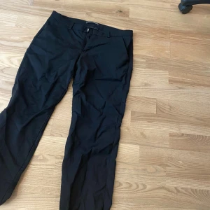 Lågmidjade bootcut kostymbyxor - Säljer ett par svarta kostymbyxor från Drykorn for beautiful people. Byxorna har lågmidjad passform, dragkedja och hällor för bälte. Perfekta till en stilren look och passar till många olika tillfällen.