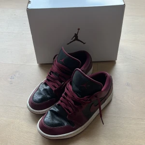 Nike Air Jordan 1 Low  - Säljer ett par Nike Air Jordan 1 Low i färgen cherrywood och svart med vita sulor. Skorna har klassisk snörning, rund tå och är tillverkade i skinn. Perfekta för dig som gillar streetwear och vill sticka ut med snygga sneakers.