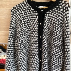 Svartvit kofta med pärlknappar  - Säljer en svartvit stickad kofta med pärlknappar framtill. Koftan har lång ärm och ett rutigt mönster. Perfekt för lager-på-lager och ger en klassisk look.