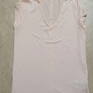 T-shirt - Säljer en ljusrosa t-shirt med korta ärmar och knappar framtill. T-shirten har en v-ringad design och är tillverkad i ett lätt och bekvämt material.