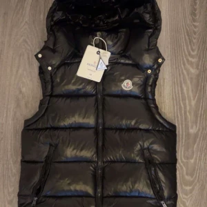  Moncler väst - Säljer en svart dunväst från Moncler med huva. Helt ny och riktigt trendig. Är storlek M men sitter som S