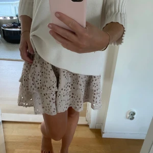 Beige volangkjol med broderade hål - Supersöt beige kjol med volanger och broderade hål som ger en luftig och somrig känsla. Kjolen är kort och har en flowy passform som sitter bekvämt i midjan. Perfekt att styla med en stickad tröja eller en enkel topp.💕Märke- Bond hour- Nypris ca 1400kr😍Mycket bra skick 